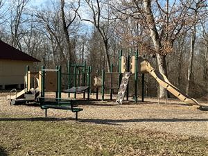playground in a wooded setting with a green bench